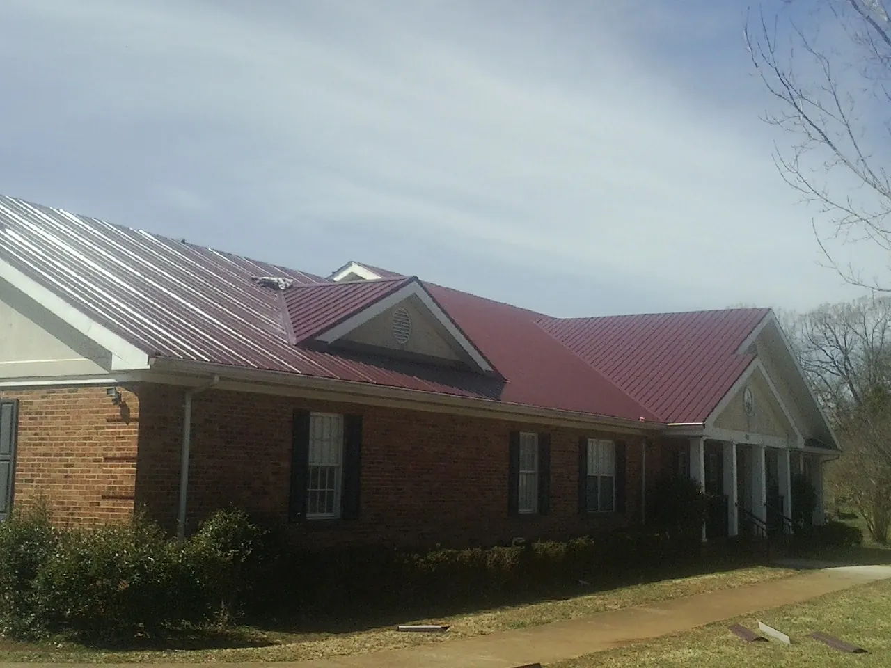 Red metal roof with gabled entries on a long brick building, from a Hail Damage Roof Repair job in Chincoteague Island