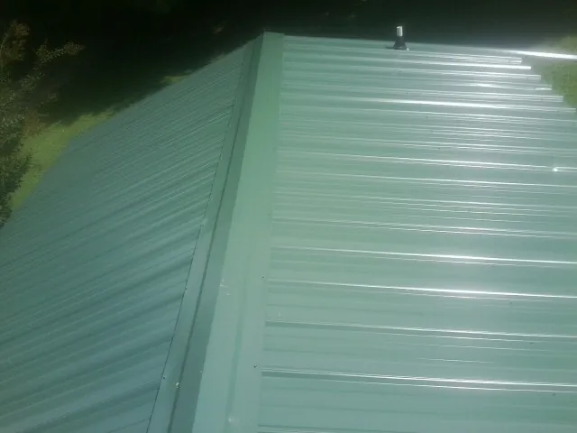 New green metal panels meeting at the ridge of a roof — Flat Roof Repair work by our crew in Chincoteague Island
