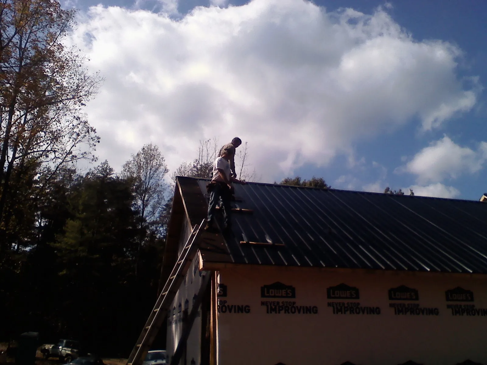 Roofer fastening dark metal panels high against a cloudy sky, from a Roof Inspection job in Chincoteague Island