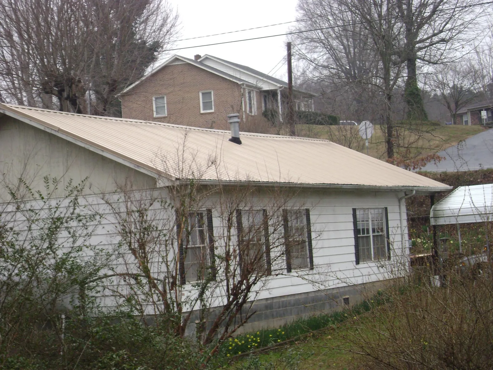 Tan metal roof on a white sided house set into a hillside — Commercial Roofing by Roofing Brothers in Chincoteague Island